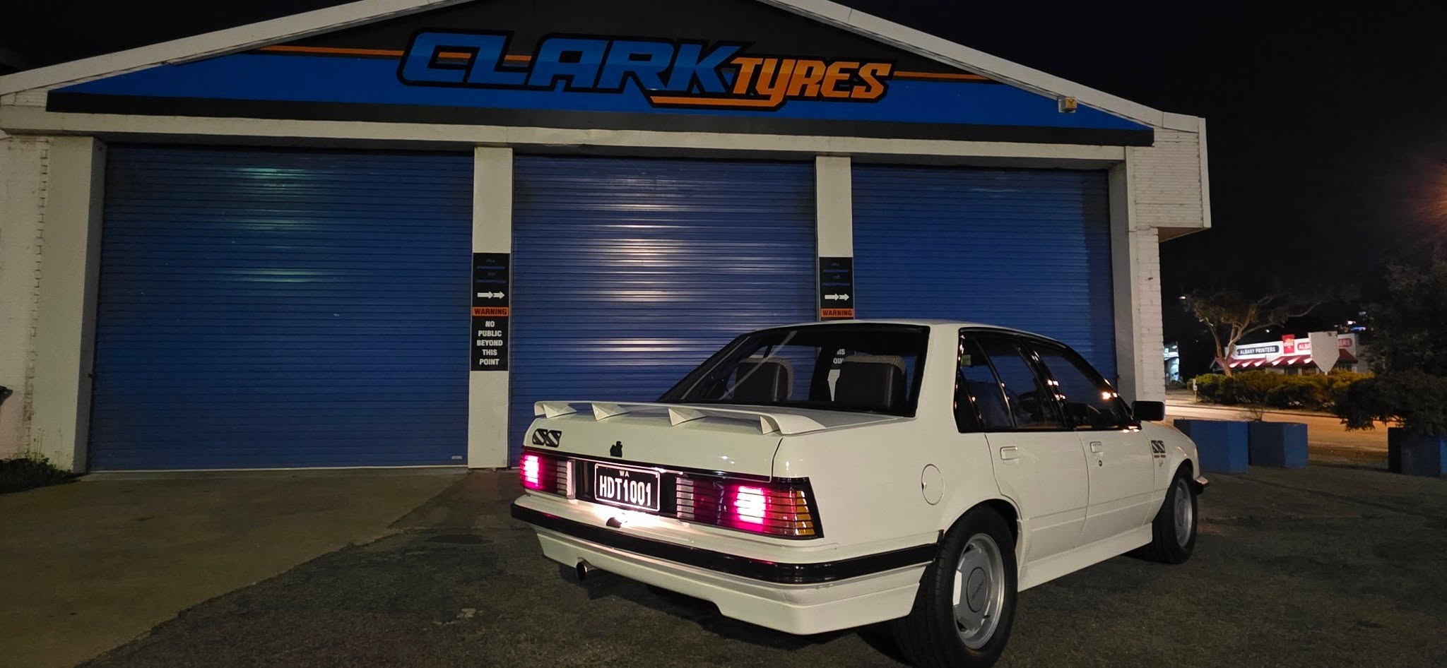 The Clark Tyres workshop at night with a classic Holden parked out the front