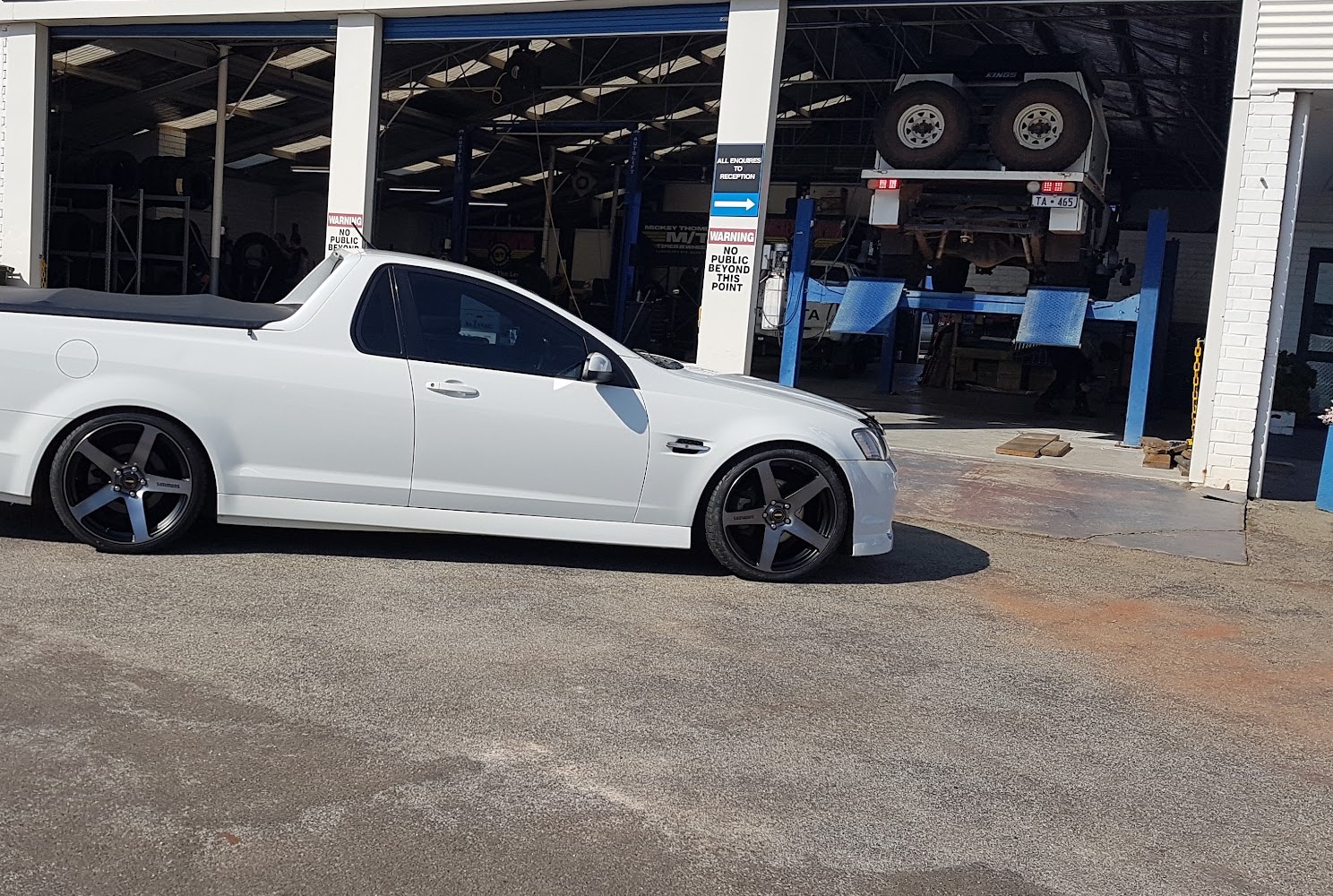 A ute on black alloy wheels on the forecourt at Clark Tyres, with a trailer up on the hoist behind